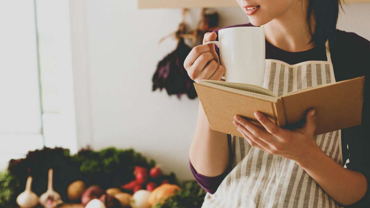 Young woman reading cookbook in the kitchen, looking for recipe .